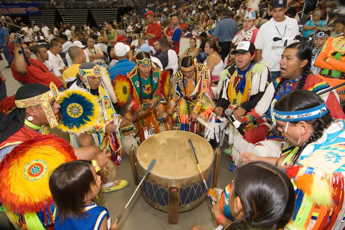 Singers and dancers in bright regalia around a large powwow drum, photographed at a Smithsonian powwow.